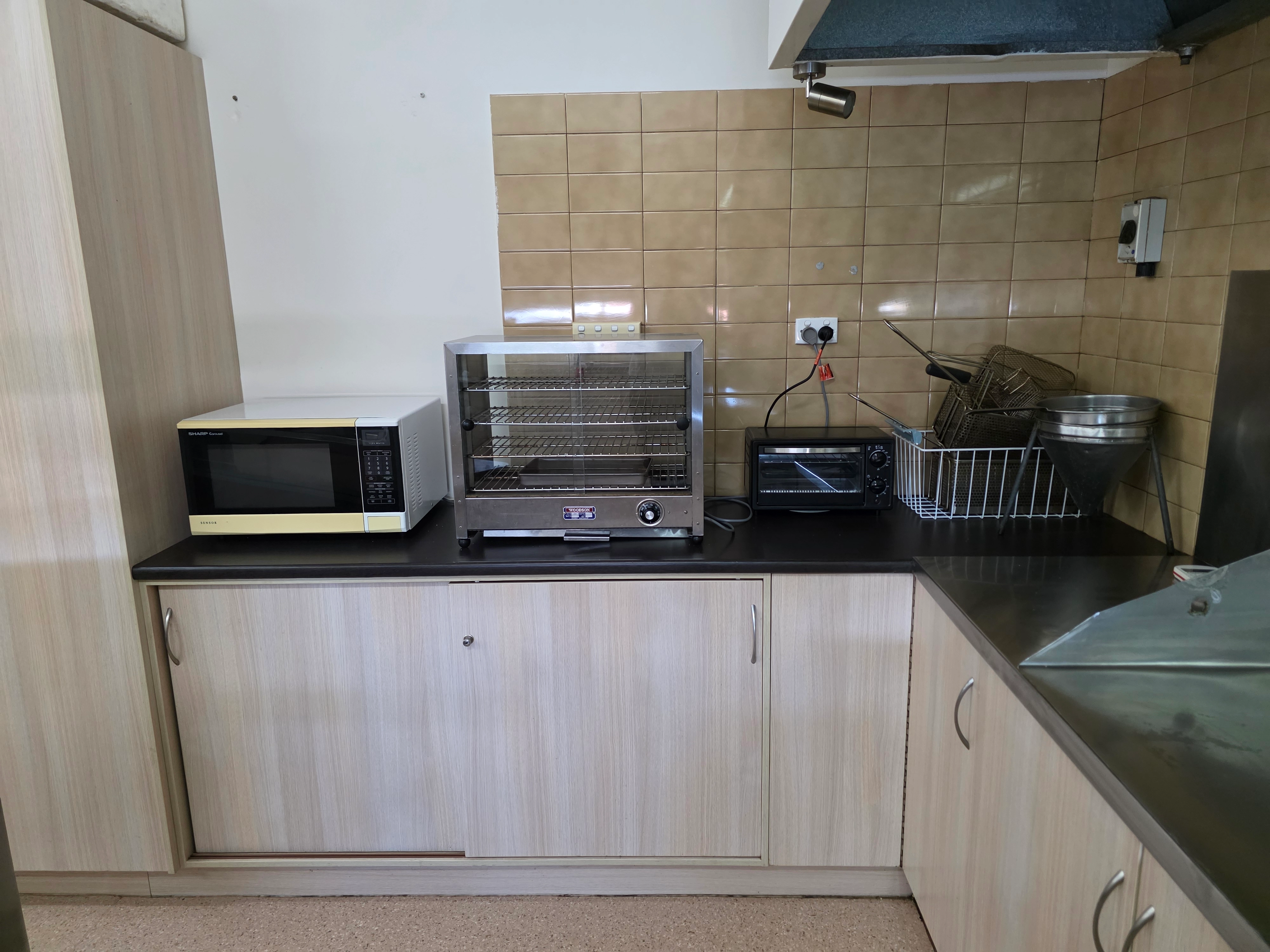 Commercial kitchen with microwave, convection oven, stainless steel benchtops and food preparation area