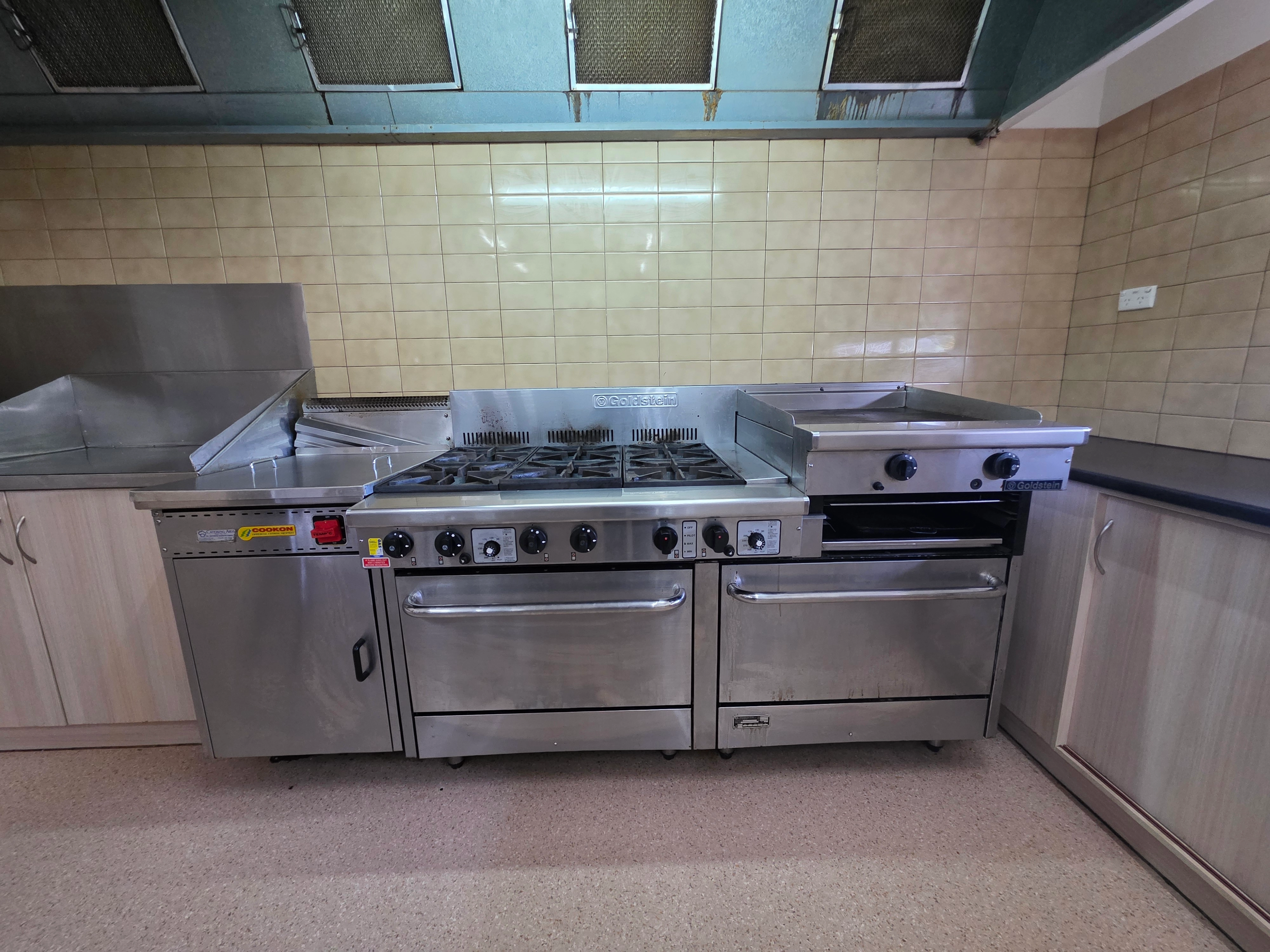 Commercial kitchen with gas cooktop, grill, stainless steel cooking equipment and preparation benches